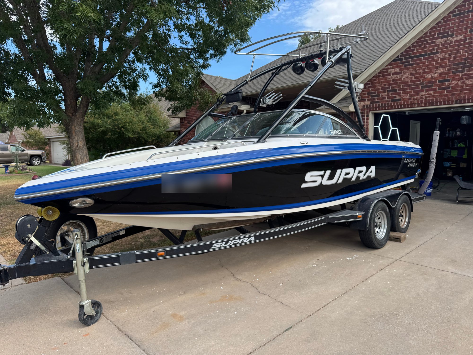 Supra wake boat on its trailer after correction, black and blue hull in full gloss