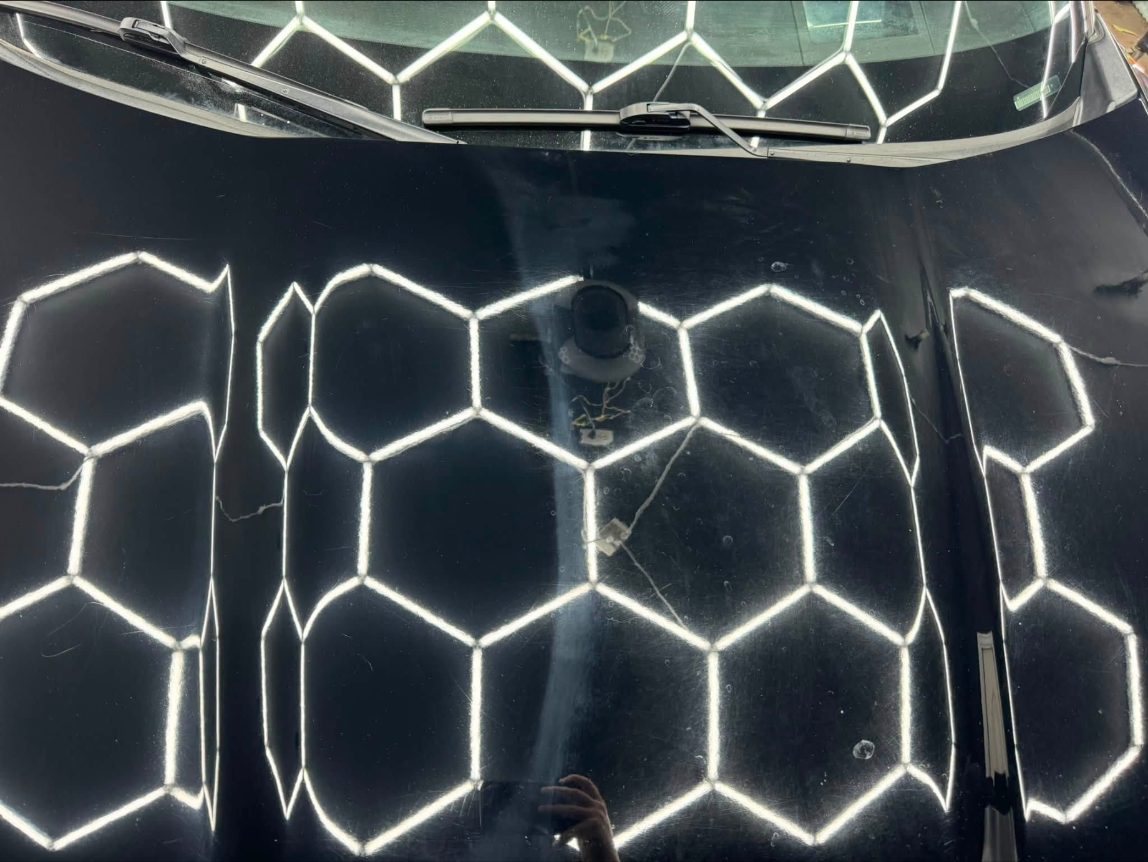 Black hood under hexagon lights showing swirl marks and scratches before correction